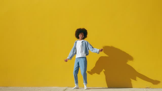 Happy young African American woman dancing and jumping on yellow background