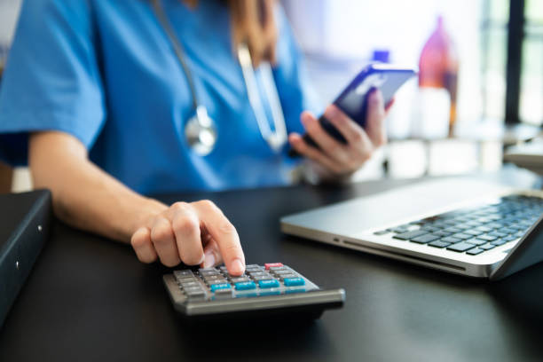 healthcare costs and fees concept.hand of smart doctor used a calculator and smartphone, tablet for medical costs at hospital in morning light - expense imagens e fotografias de stock