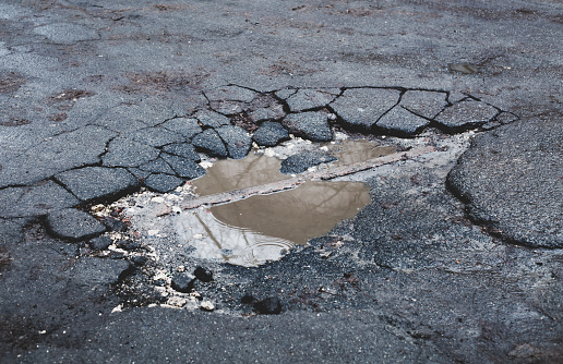paved road surface is damaged. Broken asphalt. Puddle on cracked road.