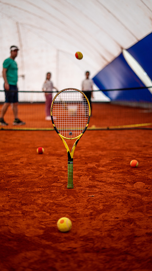 tennis racket is foreground focus on foreground kids tennis club is background clay court vertical still