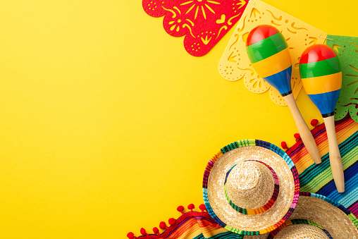 Cinco-de-mayo concept. Top view photo of traditional headwear sombrero colorful striped serape garland and couple of maracas on isolated bright yellow background with empty space