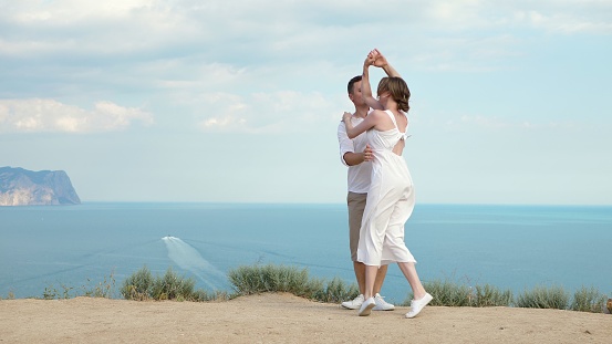 A man and a woman in love are having fun and dancing on a cliff overlooking the sea and mountains