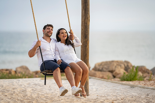 Happy couple on rope swing on tropical beach shore