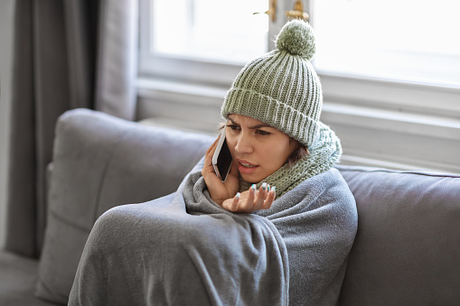 Freezing Young Woman Wrapped In Blanket Making Phone Call At Home, Stressed Female Tenant Sitting On Couch And Talking On Cellphone, Complaining About Cold Temperature In Apartment, Closeup