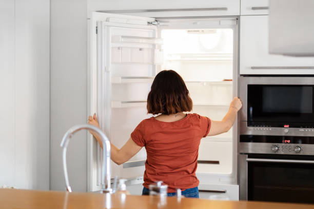 istock Young Woman Standing In Kitchen And Looking Inside Of Empty Fridge 1479050677