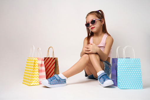 Cute little girl with shopping bags on a white background with copy space. Portrait of a child girl with colorful shopping bags, full body