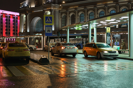 Moscow, Russia - March 26, 2023: Square of Kievsky railway station at night. Bus station, taxi parking area. Bright reflections of the city lights on wet road. Touristic concept. Street photography