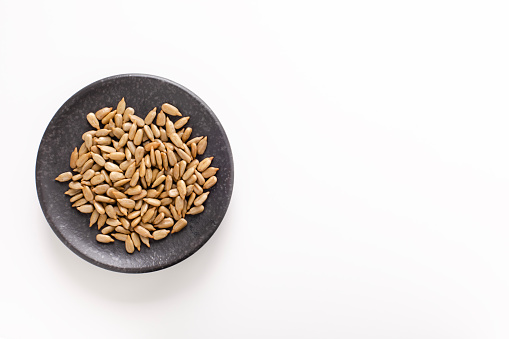 Top view of a small black plate with roasted sunflower seeds, on white background with copy space