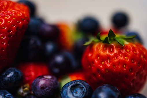 This vibrant and colorful photo showcases a bountiful harvest of ripe blueberries and strawberries. Packed with nutrition and antioxidants like vitamin C and fiber, these juicy fruits are a healthy and delicious addition to any diet. Perfect for a summer dessert or snack, these organic and natural berries are captured in stunning detail, with a rustic wooden background adding to the natural beauty of the composition. Whether you're a vegetarian, vegan, or simply appreciate fresh and tasty food, this close-up of blueberries and strawberries is sure to make your mouth water.