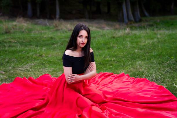 istock Young beautiful dancer female with a sad expression in a red dress posing in a park 1479065729