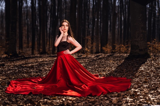 A beautiful young female in a red dress posing in an autumn forest