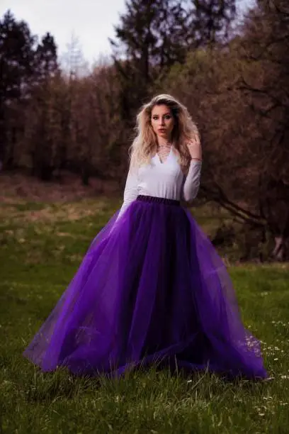 A young female posing in a white shirt and a purple tulle skirt in a park