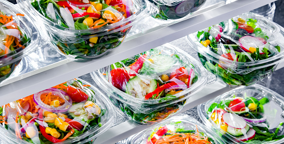 Plastic boxes with pre-packaged vegetable salads, put up for sale in a commercial refrigerator
