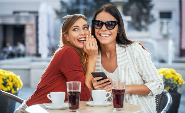 Little secrets. Two girls sitting in the cafe and whispering about pretty guy who sitting at the table next to them. Love and relationships stock photo