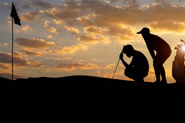 istock Golfers' hit golf ball toward the hole at sunset silhouetted 1479075319