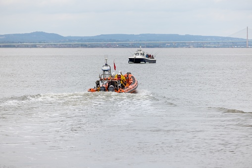 Portishead, United Kingdom – October 27, 2022: Orange lifeboat heads out to mean small pleasure vessel