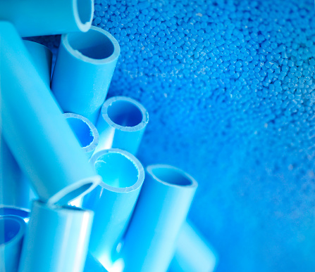 Blue pipe and plastic polymer pellets raw material for blue pvc pipe production. Industrial plastic resin. Chemical polymer granules. Thermoplastic. Plastic from petrochemical and compound extrusion.