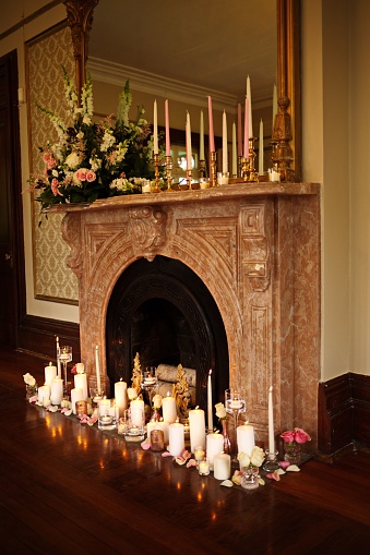 A cozy fireplace mantle decorated with an array of colorful candles and flowering plants, creating a peaceful atmosphere
