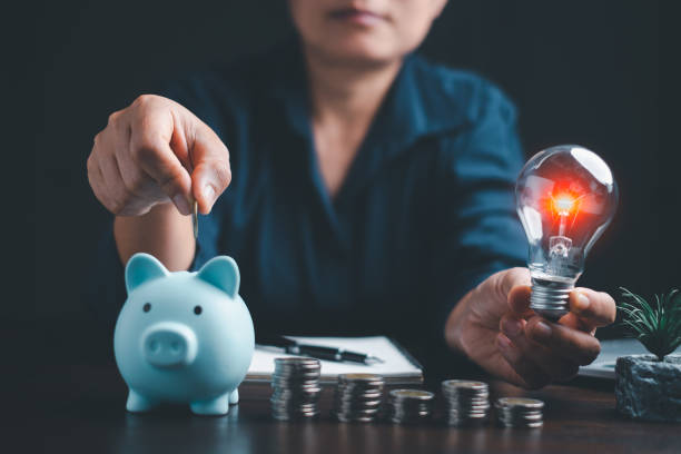 istock Businesswoman hand holding lightbulb with using calculator to calculate and money stack. Idea of energy saving planning in home. Save energy and money with accounting finance in office concept. 1479079619