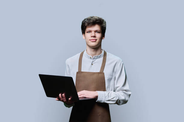 istock Young male in an apron with laptop, on gray studio background 1479079795