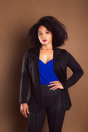 Business manager woman dressed in black blazer standing against brown background. Studio portrait.