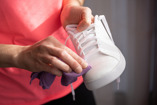 A female is cleaning a white sneaker with a purple cloth