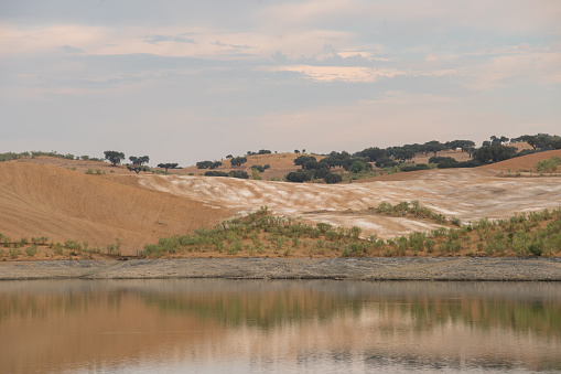 Desert like hill landscape with reflection on the water on a dam lake reservoir at sunset in Terena, Portugal