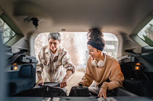 two beautiful women student mother and daughter female travel concept take luggage baggage suitcase and other stuff belongings from back of car while moving into dormitory on college campus or travel