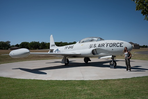 Weatherford, United States – September 15, 2022: A smiling woman stands next to an old fighter jet