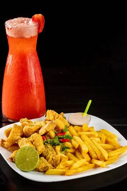 A vibrant red drink and a plate of nuggets and French fries on a black background