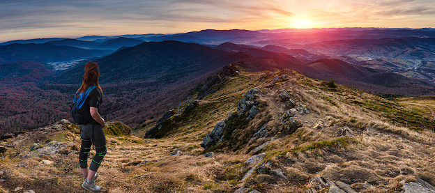 A young woman with a backpack on his back is standing in top mountain and looking at the hills in the distance. Amazing panoramic landscape mountains.