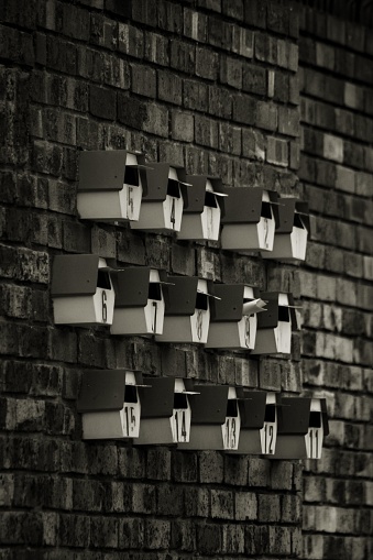 A grayscale shot of a brick wall, featuring a variety of mailboxes mounted on it