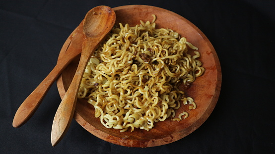 instant fried noodles with rice and  round snack topping on wooden plate isolated on black background.