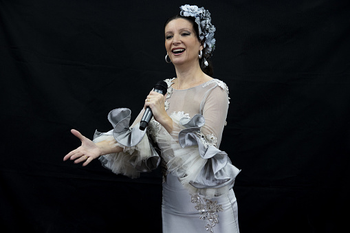 A closeup shot of a female singing with a gray Spanish costume on a black background