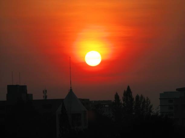 istock Sun setting behind a building in front of an orange sky 1479100624
