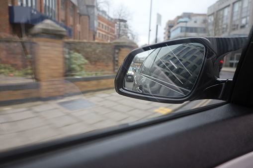 A rear view mirror in a car interior, seen from the driver's seat, as the vehicle travels down a city street