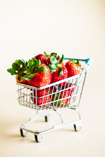 Miniature shopping cart with strawberries on a beige background.