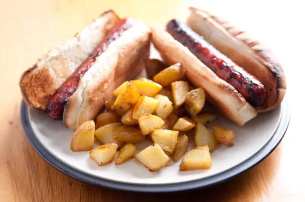 grilled hotdogs on white bread bun with ketchup and home made hash browns. This is a classic lunch meal.