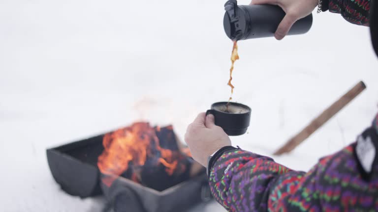 Close-up of man with thermos pouring coffee, Close-up of man drinking coffee in winter forest, Fross with hot drink, winter camper drinking hot coffee from his thermos in snowy weather, hot coffee with campfire