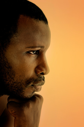 Portrait of a worried man with dark skin, head in hand, profile view, light orange background, photo