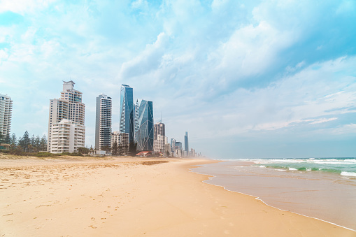 Spectacular wide panorama of the Gold Coast skyline and the rolling waves of the Pacific Ocean at Surfers Paradise beach on a cloudy summer day, Queensland, Australia.