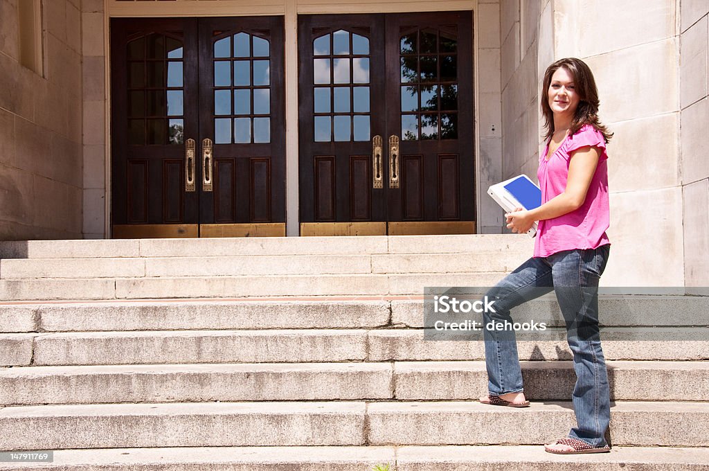 Aluna em pé na escola porta com manuais escolares - Foto de stock de 20 Anos royalty-free