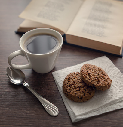 Still life. White cup with coffee and cookies in front of an open book with poetry