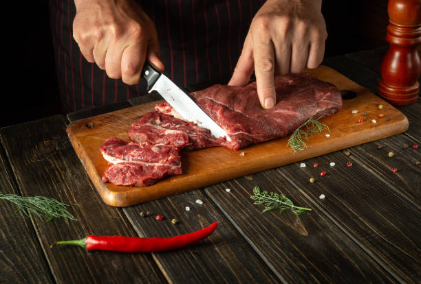 istock Butcher or chef cuts raw fresh beef meat on a cutting board before baking or barbecue. Working environment in the kitchen of a restaurant or hotel. 1479130144