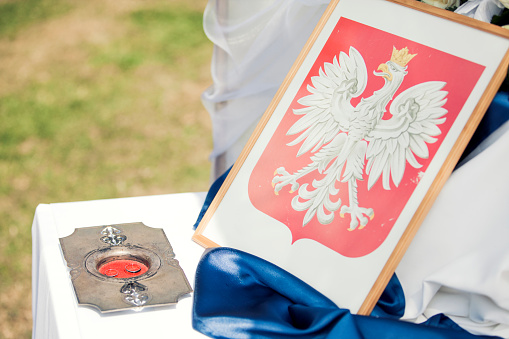 Close-up of an outdoor civil wedding setting - official table, Polish emblem and wedding rings on a silver platter.