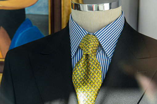 Male mannequin wearing elegant black suit and yellow tie, in a men's boutique.