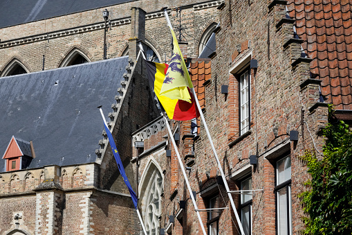 Bruges, Belgium - September 12, 2022: Flagpoles have been attached to the brick facade of the historic building. There are: the flag of Europe, the flag of Belgium and the flag of the Flemish Region