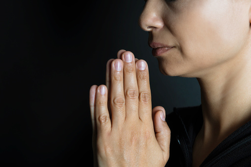 Side view of praying woman with black background.