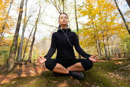 Caucasian female is meditating in forest with eyes closed.