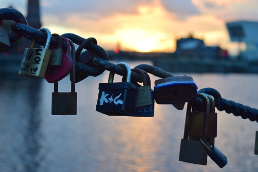 Liverpool, Merseyside, United Kingdom: Love locks on a fence at the Liverpool canning dock with a vibrant sunset reflecting on the water